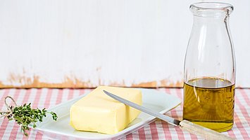 Hier sehen Sie Butter und eine Flasche mit Öl, die auf dem Tisch stehen.