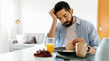 Ein Mann sitzt am Tisch und hat nach dem Essen ein Völlegefühl und Blähungen
