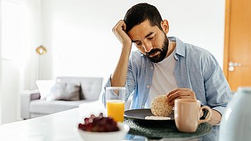 Ein Mann sitzt am Tisch und hat nach dem Essen ein Völlegefühl und Blähungen