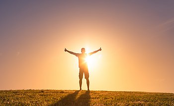 Ein Mann steht mit ausgebreiteten Armen mit einem positiven Lebensgefühl vor der Abendsonne