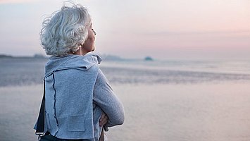 Seniorin mit Bauchspeicheldrüsenschwäche blickt über das Meer zum Sonnenuntergang