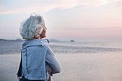 Seniorin mit Bauchspeicheldrüsenschwäche blickt über das Meer zum Sonnenuntergang