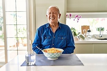 Ein älterer sitzt am Tisch und ißt Spaghetti und hält sich dabei mit schmerzverzehrtem Gesicht den Bauch.