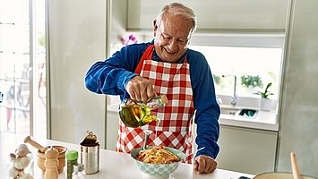 Ein älterer Herr gibt gutes Olivenöl zu seinen Spaghetti