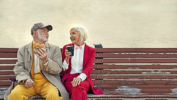 Ein älteres Ehepaar sitzt auf einer Parkbank mit einem Burger und einem Latte Machiatto und genießt das Essen trotz Bauchspeicheldrüsenschwäche (exokrine Pankreasinsuffizienz).