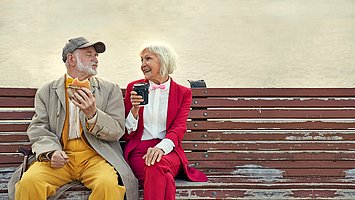 Ein älteres Ehepaar sitzt auf einer Parkbank mit einem Burger und einem Latte Machiatto und genießt das Essen trotz Bauchspeicheldrüsenschwäche (exokrine Pankreasinsuffizienz).